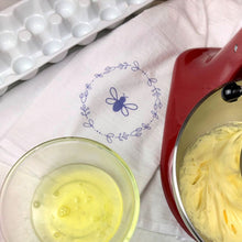 Load image into Gallery viewer, A natural coloured flour-bag cotton tea towel printed with a lavender Bee surrounded by a wreath of flowers graphic: L'Abeille Française