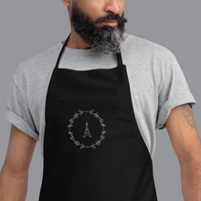 Load image into Gallery viewer, Bib of a black canvas apron with a graphic of the Eiffel Tower surrounded by a wreath of flowers embroidered in silver thread: L'Abeille Française