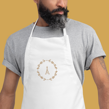 Load image into Gallery viewer, Bib of a white canvas apron with a graphic of the Eiffel Tower surrounded by a wreath of flowers embroidered in gold thread: L'Abeille Française