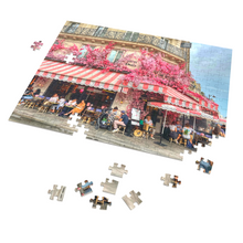 Load image into Gallery viewer, A 252-piece 14" × 11" jigsaw puzzle of the Restaurant La Favorite in Paris bedecked in pink and white striped awnings and festooned with an abundance of pink flowers.
