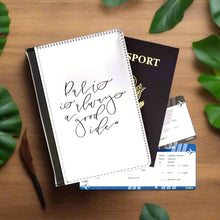 Load image into Gallery viewer, The white front cover of a faux leather passport holder is printed with a black script saying 'Paris is always a good idea' and has a black spine.