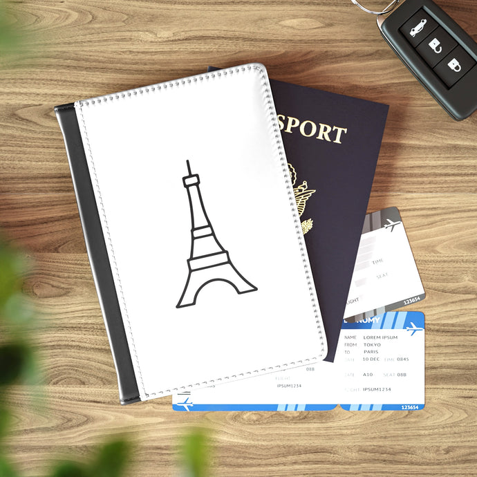 The white front cover of a faux leather passport cover is printed with a graphic of the Eiffel Tower in black and has a black spine.
