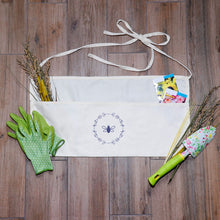 Load image into Gallery viewer, Natural-coloured garden apron with three pockets, two ties and a lavender bee and wreath graphic
