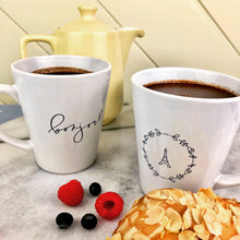 Load image into Gallery viewer, This white latte mug comes with two lavender coloured graphics printed on it, with "bonjour" one one side and the Effiel Tower surrounded by a wreath of flowers on the other: L'Abeille Française