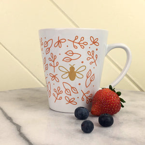 Busy Bee Latte Mug - wrap-around graphic of a gold bee surrounded by rose gold flowers on a white latte mug