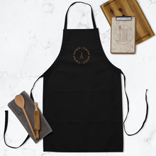 Load image into Gallery viewer, A black canvas apron with a graphic of the Eiffel Tower surrounded by a wreath of flowers embroidered in gold thread: L'Abeille Française