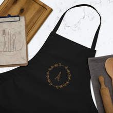 Load image into Gallery viewer, Bib of a black canvas apron with a graphic of the Eiffel Tower surrounded by a wreath of flowers embroidered in gold thread: L'Abeille Française