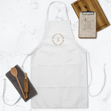 Load image into Gallery viewer, A white canvas apron with a graphic of the Eiffel Tower surrounded by a wreath of flowers embroidered in gold thread: L'Abeille Française