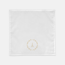Load image into Gallery viewer, White cloth napkin with a gold graphic of the Eiffel Tower surrounded by a wreath of flowers: L'Abeille Française
