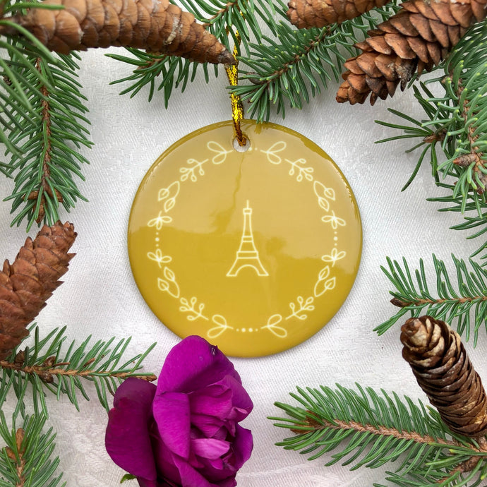 Glossy, round, gold-coloured ceramic ornament with a lighter gold-toned Eiffel Tower and wreath motif