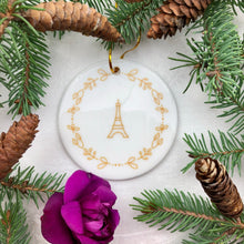Load image into Gallery viewer, Glossy, round, white ceramic ornament decorated with a gold-toned Eiffel Tower and wreath motif