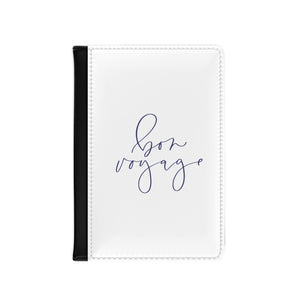 The white front cover of a faux leather passport holder is printed with a lavender coloured script saying 'bon voyage' and has a black spine.