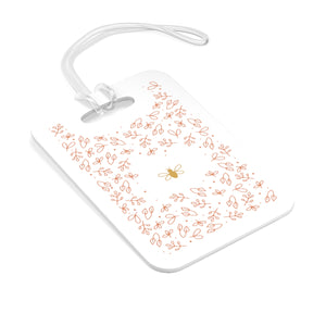 Hard, white plastic luggage tag with gold bee surrounded by pink flowers printed on it