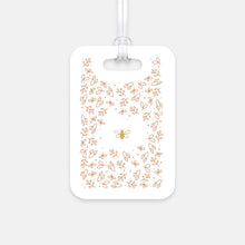 Load image into Gallery viewer, Hard, white plastic luggage tag with gold bee surrounded by pink flowers printed on it