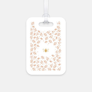 Hard, white plastic luggage tag with gold bee surrounded by pink flowers printed on it