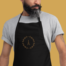 Load image into Gallery viewer, Bib of a black canvas apron with a graphic of the Eiffel Tower surrounded by a wreath of flowers embroidered in gold thread: L&#39;Abeille Française