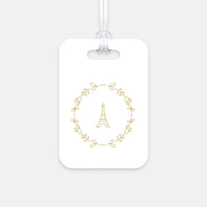 Hard, white plastic luggage tag with a graphic of the Eiffel Tower surround by a wreath of flowers printed on it in gold