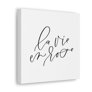 A 10" x 10" square white canvas with the phrase 'la vie en rose' printed on it in a contemporary caligraphic script: L'Abeille Française