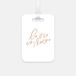 Hard, white plastic luggage tag with La Vie En Rose written on it in a rose gold script
