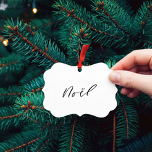 Load image into Gallery viewer, Hand holding a &#39;Noél&#39; ornament against a Christmas tree background