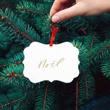 Load image into Gallery viewer, Hand placing a &#39;Noél&#39; ornament on a Christmas tree.