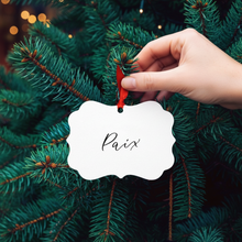 Load image into Gallery viewer, Hand placing a &#39;Paix&#39; ornament on a Christmas tree branch