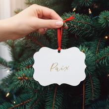 Load image into Gallery viewer, Hand hanging a Christmas ornament with &#39;Paix&#39; on a decorated tree