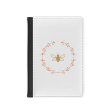 Load image into Gallery viewer, The white front cover of a faux leather RFID passport cover is printed with a peach &amp; gold graphic of a bee surrounded by a wreat of flowers and has a black spine.