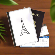 Load image into Gallery viewer, The white front cover of a faux leather passport cover is printed with a graphic of the Eiffel Tower in black and has a black spine.