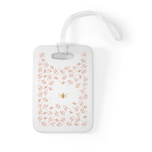 Hard, white plastic luggage tag with gold bee surrounded by pink flowers printed on it 