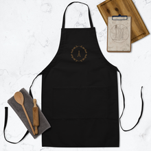 Load image into Gallery viewer, A black canvas apron with a graphic of the Eiffel Tower surrounded by a wreath of flowers embroidered in gold thread: L&#39;Abeille Française
