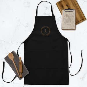 A black canvas apron with a graphic of the Eiffel Tower surrounded by a wreath of flowers embroidered in gold thread: L'Abeille Française