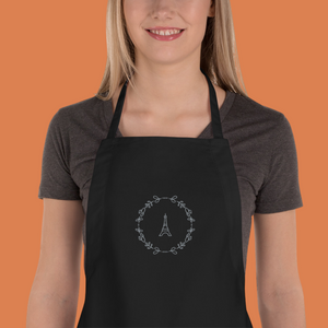Bib of a black canvas apron with a graphic of the Eiffel Tower surrounded by a wreath of flowers embroidered in silver thread: L'Abeille Française
