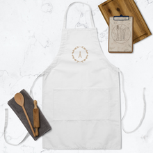 Load image into Gallery viewer, A white canvas apron with a graphic of the Eiffel Tower surrounded by a wreath of flowers embroidered in gold thread: L&#39;Abeille Française