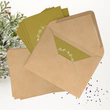 Load image into Gallery viewer, A set of seven gold rectangular Christmas postcards with a wreathed Eiffel Tower graphic and the phrase Joyeux Noel printed in off-white accomanied by coordinating  kraft paper envelopes.