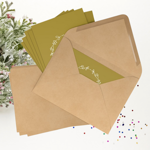 A set of seven gold rectangular Christmas postcards with a wreathed Eiffel Tower graphic and the phrase Joyeux Noel printed in off-white accomanied by coordinating  kraft paper envelopes.