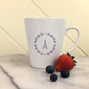 Bonjour Eiffel Latte Mug: lavender graphic of the Eiffel Tower surrounded by a wreath of flowers on a white latte mug