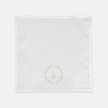 Load image into Gallery viewer, White cloth napkin with a gold graphic of the Eiffel Tower surrounded by a wreath of flowers: L&#39;Abeille Française