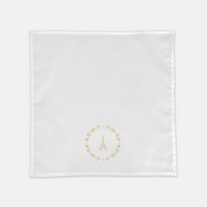 White cloth napkin with a gold graphic of the Eiffel Tower surrounded by a wreath of flowers: L'Abeille Française