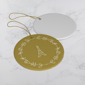 Glossy, round, gold-coloured ceramic ornament with a lighter gold-toned Eiffel Tower and wreath motif lying next to the white back of another