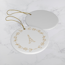 Load image into Gallery viewer, Glossy, round, white ceramic ornament decorated with a gold-toned Eiffel Tower and wreath motif lying next to the white back of another
