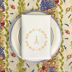 White cloth napkin with a gold graphic of the Eiffel Tower surrounded by a wreath of flowers: L'Abeille Française