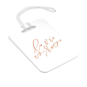 Hard, white plastic luggage tag with La Vie En Rose written on it in a rose gold script