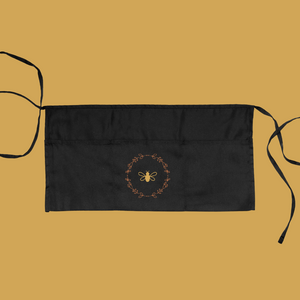 Black garden apron with three pockets, two ties and a gold bee and wreath graphic