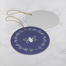 Load image into Gallery viewer, Glossy, round, lavender-coloured ceramic ornament with a white bee and wreath motif next to the white back of another