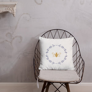 A white cushion with a gold bee surrounded by a lavender flower wreath graphic sitting on a wire chair